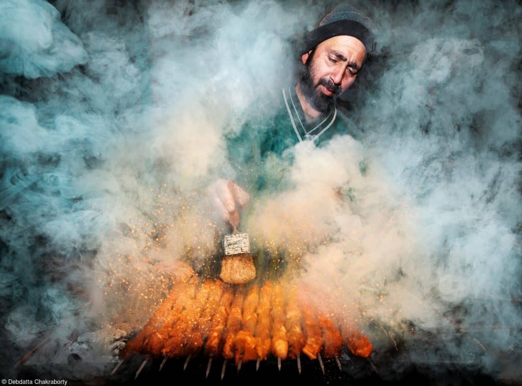 A street vendor fires up charcoal ovens and smoke fills the air 